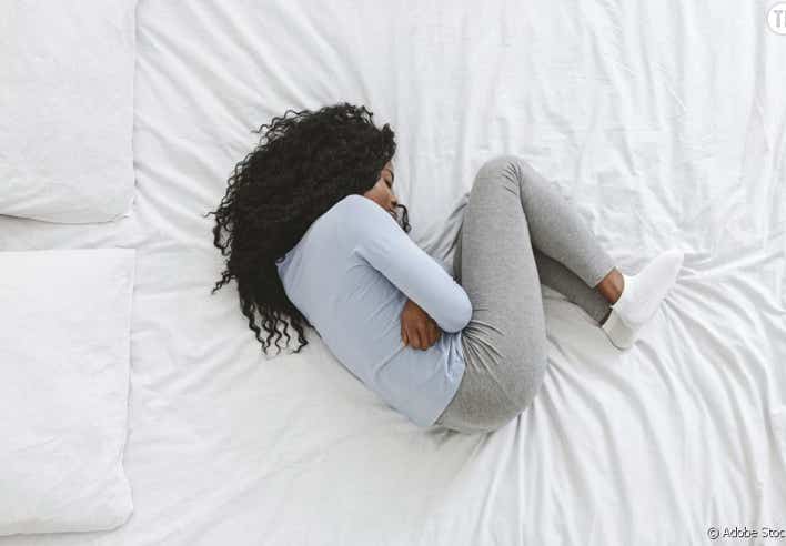 Femme allongée en position fœtale sur un lit, illustrant les douleurs menstruelles apaisées par l’acupression proposée au cabinet Terre de Shiatsu Lyon 5e pour soulager les crampes et rétablir l’équilibre hormonal.