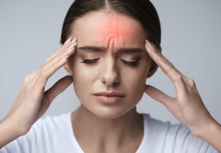 Femme souffrant d’une migraine, les yeux fermés et les mains sur les tempes, avec une zone rouge marquant la douleur au front. Cette image illustre un soin proposé par le cabinet Terre de Shiatsu Lyon 5e, où le massage migraine soulage efficacement les tensions crâniennes et réduit la fréquence des crises.