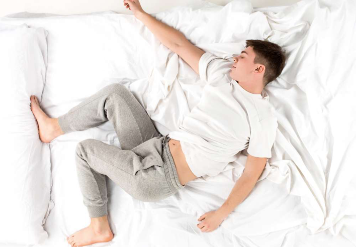 Homme dormant en position désorganisée sur un lit défait, illustrant un sommeil agité ou non réparateur. Cette image évoque les troubles du repos nocturne et met en valeur les bienfaits d’un massage sommeil au cabinet Terre de Shiatsu Lyon 5e, visant à détendre le corps et apaiser l’esprit pour un sommeil plus profond et récupérateur.