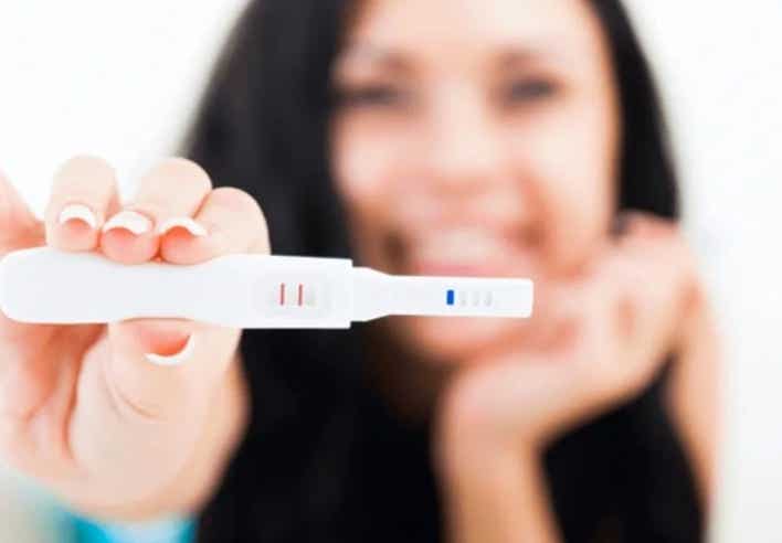 Image d’une femme souriante tenant un test de grossesse positif, illustrant les bienfaits du massage pour la fertilité proposé par le cabinet Terre de Shiatsu Lyon 5e.