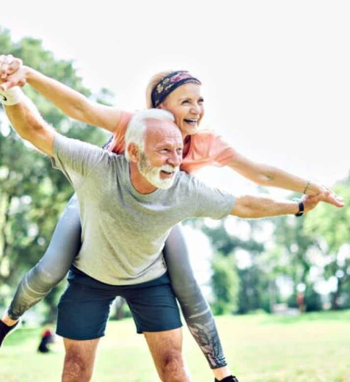 Couple de personnes agées en plein vitalité dans un parc avec la femme sur le dos de l'homme, symbolisant la revitalisation du corps et la stimulation de la vitalité par le Shiatsu - cabinet Terre de Shiatsu Lyon 5e