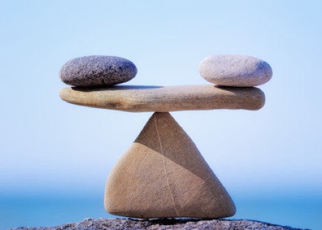 Une pierre blanche et noire posées chacune à une extrémité d'une pierre plate qui est en équilibre sur une pointe d'une pierre triangulaire, représentant l'équilibre énergétique du corps  grâce au massage Chi Nei Tsang - cabinet Terre de Shiatsu Lyon 5e