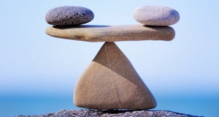 Une pierre blanche et noire posées chacune à une extrémité d'une pierre plate qui est en équilibre sur une pointe d'une pierre triangulaire, représentant l'équilibre énergétique - cabinet Terre de Shiatsu Lyon 5e