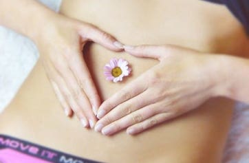 Ventre d'une femme allongée sur le dos mettant ses mains en forme de coeur autour de son nombril sur lequel est posée une fleur, symbolisant le rééquilibre des fonctions internes - cabinet Terre de Shiatsu Lyon 5e