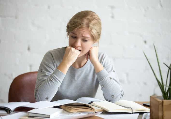 Femme stressée se mordant sa main droite face à des documents, illustrant l’anxiété liée au stress — soin en Shiatsu au cabinet Terre de Shiatsu Lyon 5e.