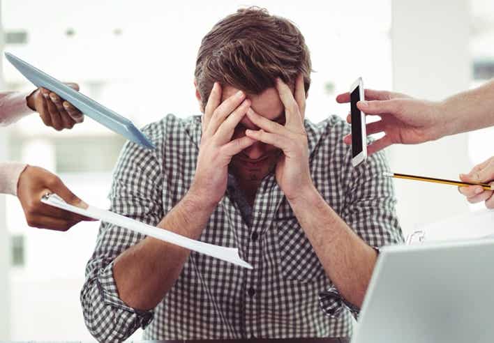 Homme débordé au bureau, visage entre les mains, submergé par les sollicitations — illustration du stress chronique et des tensions mentales soulagées par un massage détoxifiant au cabinet Terre de Shiatsu Lyon 5e.