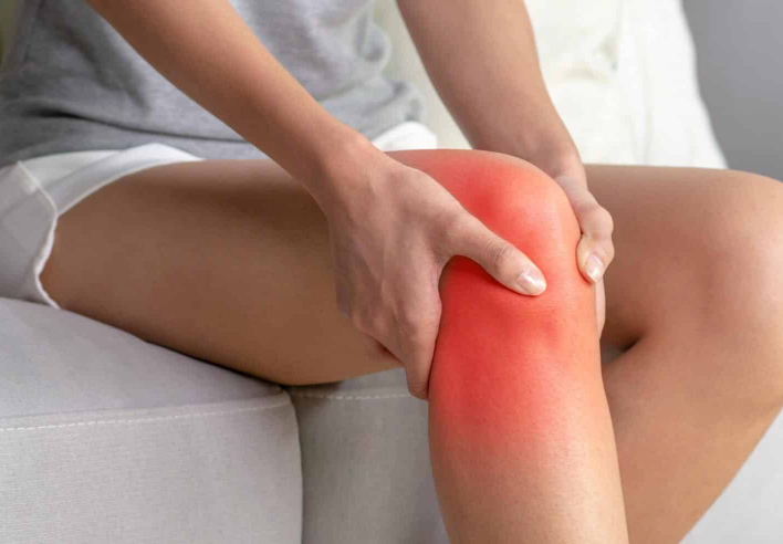 Personne assise tenant son genou avec les deux mains, une zone rouge signalant une douleur articulaire, illustrant l’action du shiatsu pour soulager les douleurs du genou et améliorer la mobilité - cabinet Terre de Shiatsu Lyon 5e