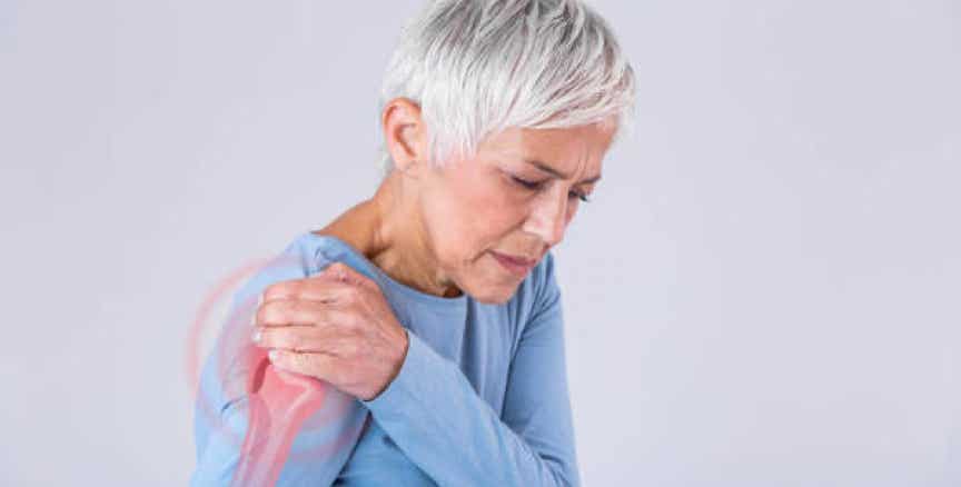 Femme senior touchant son épaule avec une expression de douleur, illustrant une inflammation articulaire ou une gêne musculaire, symbole des douleurs articulaires soulagées par le shiatsu - Cabinet Terre de Shiatsu Lyon 5e