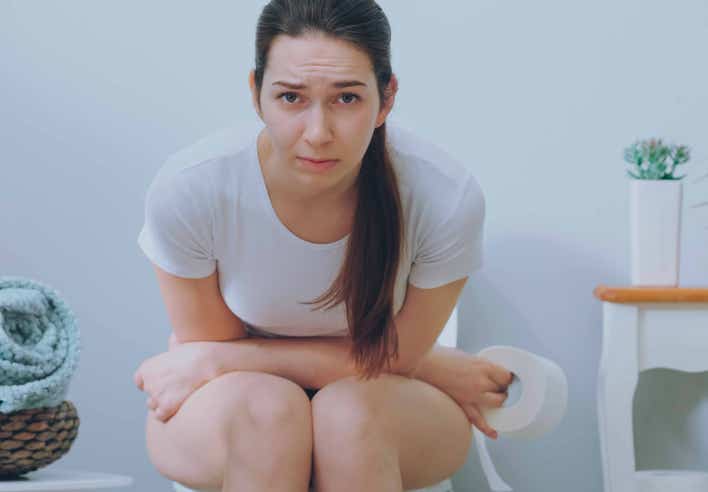 Femme assise aux toilettes avec une expression de gêne, tenant un rouleau de papier toilette. L’image illustre de façon explicite l’inconfort lié à la constipation. Cette situation est en lien avec les bienfaits d’un massage pour la constipation proposé au cabinet Terre de Shiatsu Lyon 5e, visant à réguler le transit et favoriser un retour au confort digestif.