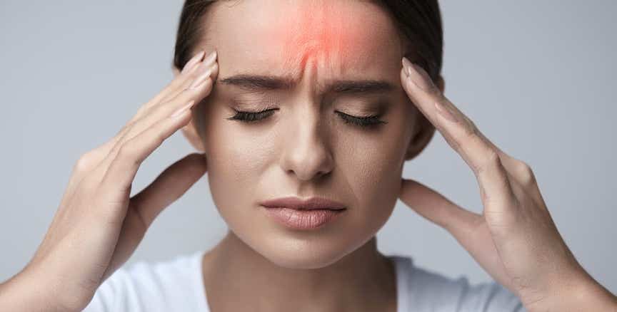 Femme souffrant de maux de tête, les mains posées sur les tempes, avec une zone rouge sur le front illustrant une migraine — soulagement des douleurs crâniennes par le Shiatsu - Cabinet Terre de Shiatsu Lyon 5e