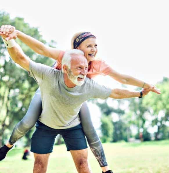 Couple de personnes agées en plein vitalité dans un parc avec la femme sur le dos de l'homme, symbolisant la libération des blocages physiques et mentaux du massage métamorphique - cabinet Terre de Shiatsu Lyon 5e