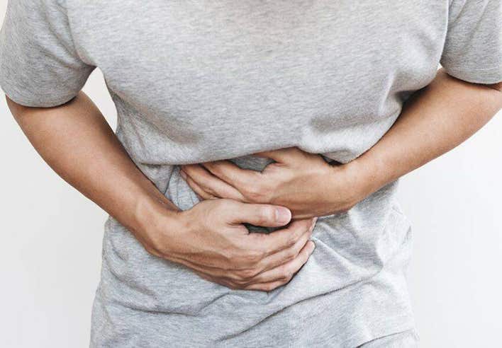 Homme en t-shirt gris se tenant le ventre avec les deux mains, manifestant une douleur abdominale intense. Cette image illustre le massage ciblé pour les coliques proposé par le cabinet Terre de Shiatsu Lyon 5e, une technique manuelle douce pour apaiser les crampes et rétablir le confort digestif.