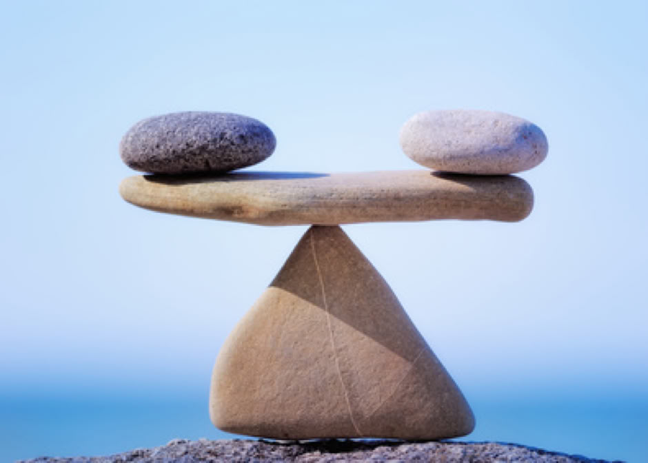 Une pierre blanche et noire posées chacune à une extrémité d'une pierre plate qui est en équilibre sur une pointe d'une pierre triangulaire, représentant l'équilibre énergétique du corps  grâce au massage Chi Nei Tsang - cabinet Terre de Shiatsu Lyon 5e