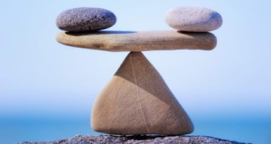Une pierre blanche et noire posées chacune à une extrémité d'une pierre plate qui est en équilibre sur une pointe d'une pierre triangulaire, représentant l'équilibre énergétique - cabinet Terre de Shiatsu Lyon 5e