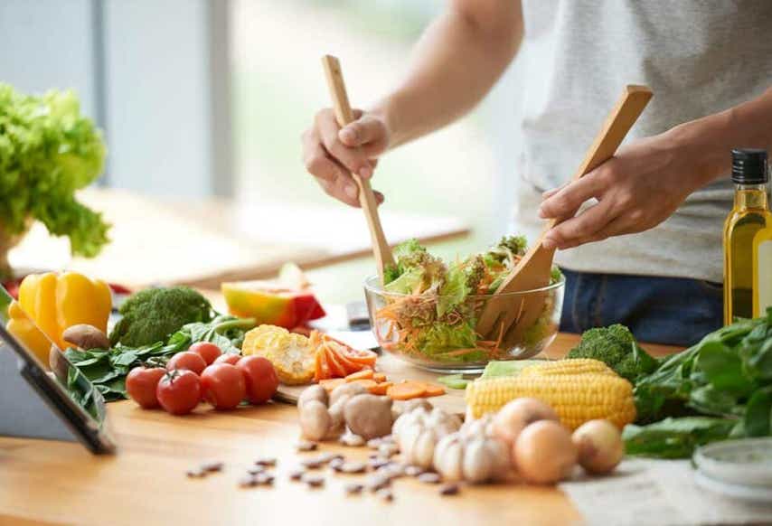 Aliments bruts étalés sur un plan de travail de cuisine avec une personne mélangeant une salade dans un saladier transparent illustrant une bonne hygiène de vie - cabinet Terre de Shiatsu Lyon 5e